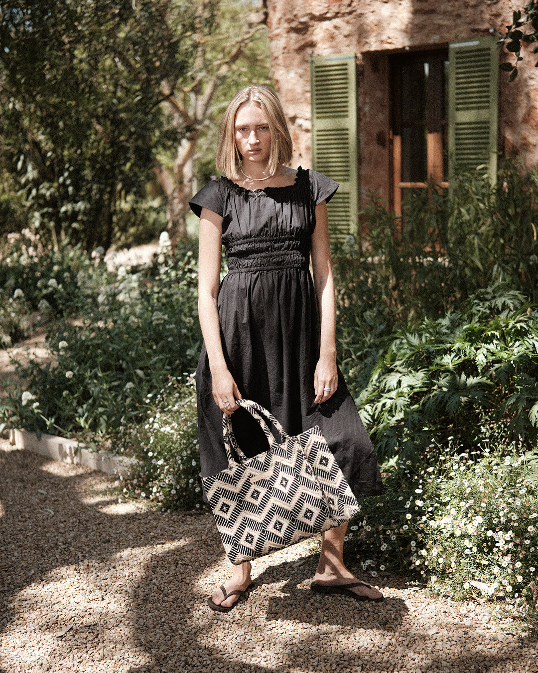 Women's black smocked midi dress with cap sleeves, paired with the black la rambla geometric tote bag. A lightweight and stylish outfit perfect for summer fashion and everyday wear.