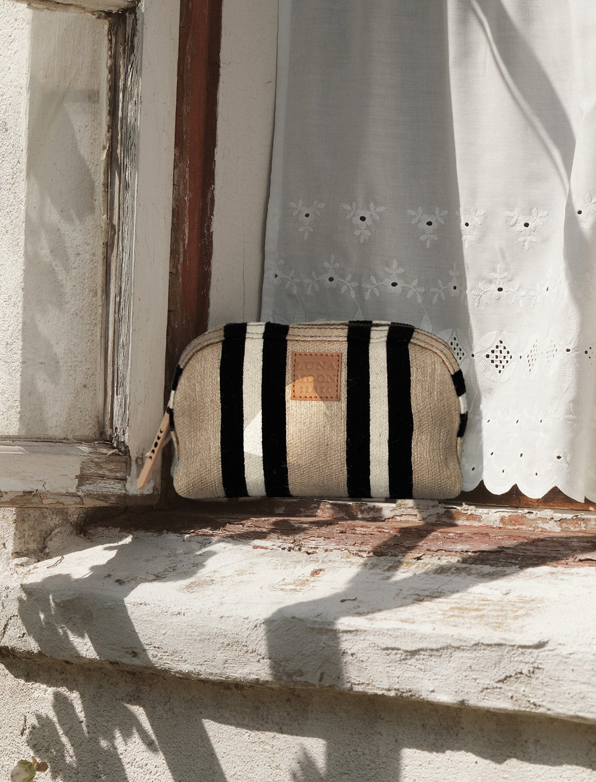 Handwoven striped pouch bag in black and beige with a zip closure and leather brand zipper. Stylish and compact, perfect for travel, cosmetics, and everyday essentials.