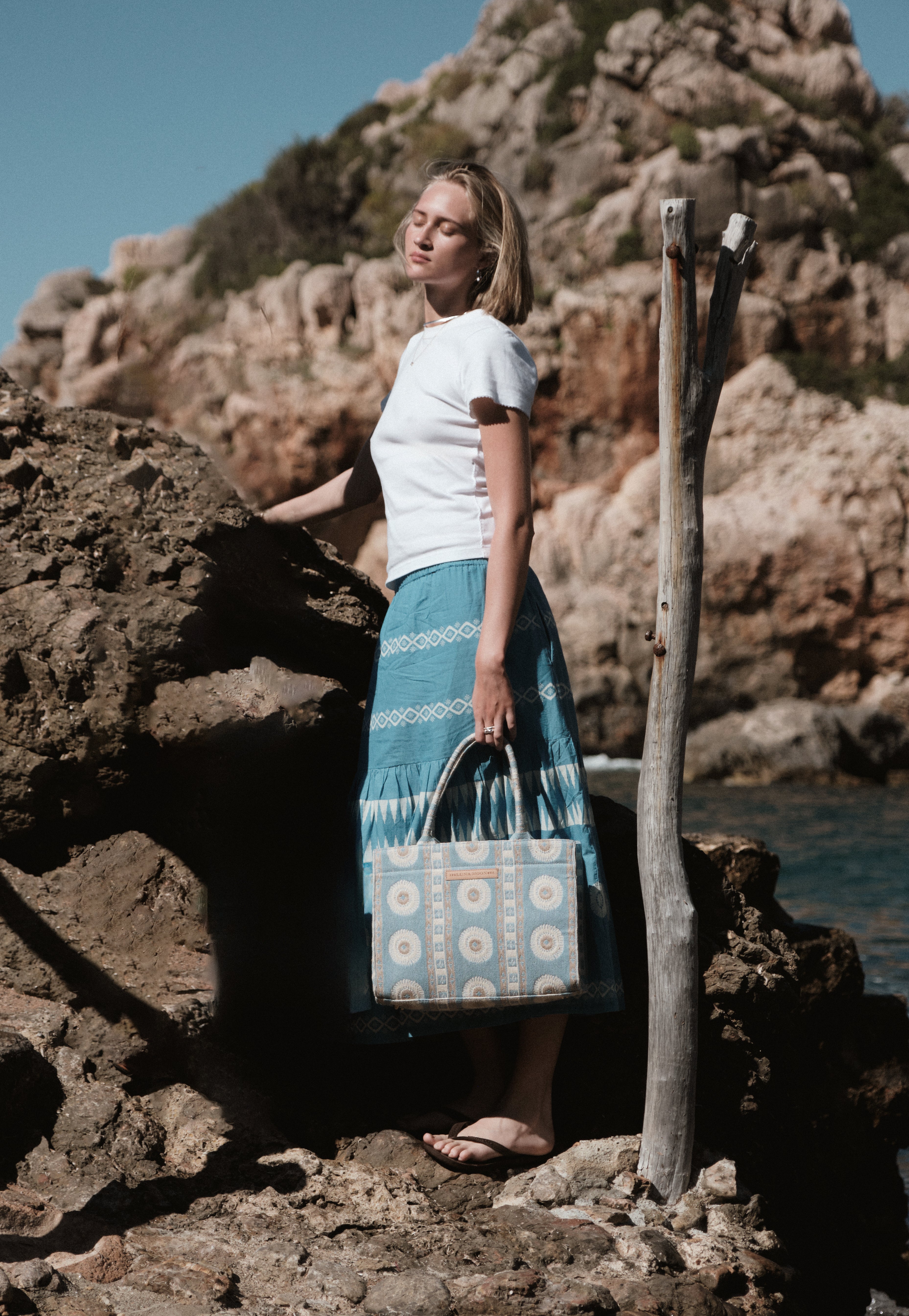 Women's bohemian blue embroidered tiered maxi skirt. Accessorized with the woven blue and beige geometric palma tote bag. A stylish and lightweight outfit perfect for summer fashion and beachwear.